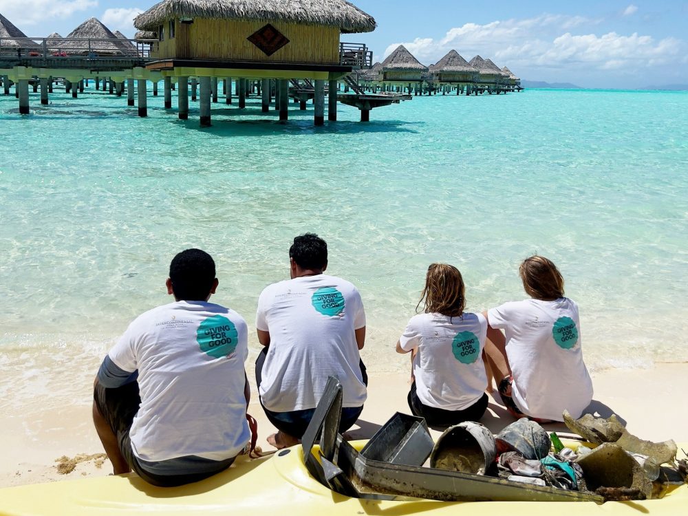 The Green Leaders team, composed of four people, sitting on a kayak and looking in the direction of the pilings of the InterContinental Le Moana Hotel